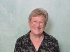 Anneke Stevens. Ze heeft kort, grijs haar, ze lacht en draagt een zwarte blouse met giraffen erop. Ze draagt een bril.