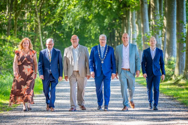 College van burgemeester en wethouders lopen over een pad tussen bomen door. Van links naar rechts: gemeentesecretaris Janneke Beikes, wethouder Ronald Bakker, wethouder Joop Slomp, burgemeester Jan Zwiers, wethouder Rico Schans en wethouder Daan de Kruijf.