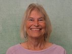 Alice Miener. Ze heeft halflang haar, draagt een roze trui en lacht.