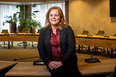 Gemeentesecretaris Janneke Beikes zittend op een tafel in de raadzaal.