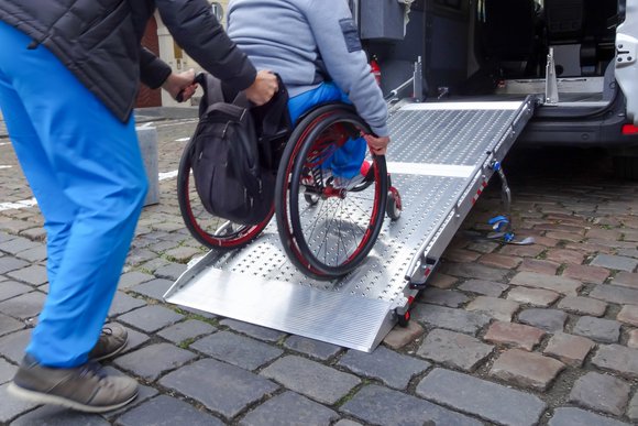 Foto van een rolstoelgebruiker die geholpen wordt een busje in te komen