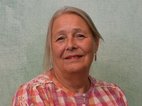 Hendriette Wijnholts. Ze draagt haar haar vast en draagt oorbellen. Ze heeft een rood-wit geruite blouse aan met een bloemenmotief op de mouwen.